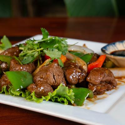 Shaking beef with peppers served with dipping sauce on a white plate.
