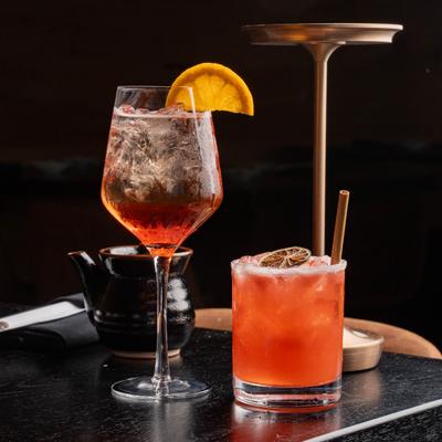 Aperol Spritz garnished with a slice of orange, served alongside a cocktail in rocks glass.