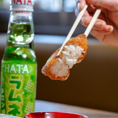 Fried tofu pouch held with chopsticks above a dipping sauce dish.