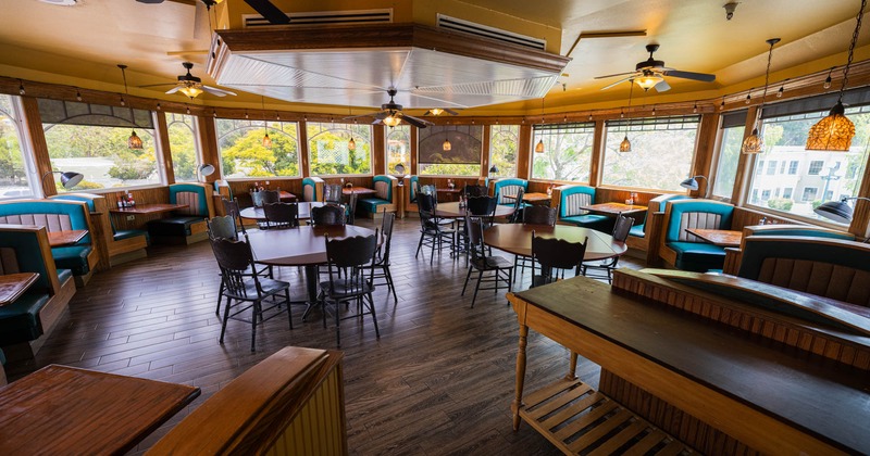 Spacious diner with wooden floors and teal-upholstered booths, Large windows offer a view of trees