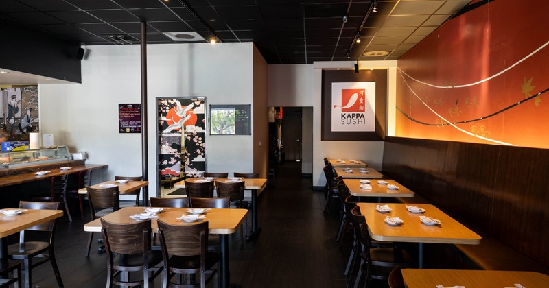 Interior of a modern sushi restaurant with wooden tables, a sushi bar, and a mural