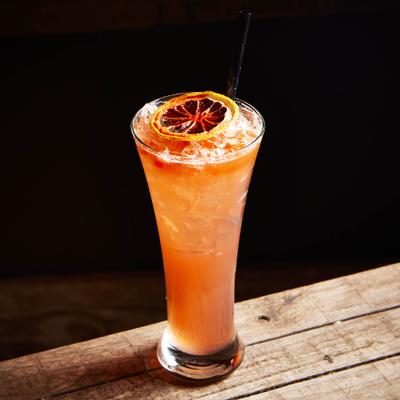 An orange cocktail drink served in a Pilsner glass with a dry citrus wheel.