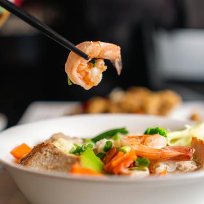 Chopsticks with a piece of shrimp above the bowl of Wor Wonton Soup.