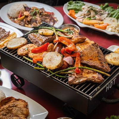 A tabletop grill, laden with mixed grill, surrounded by assorted food plates.