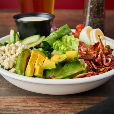 Cobb salad with avocado, bacon, egg, blue cheese, and a side of dressing.