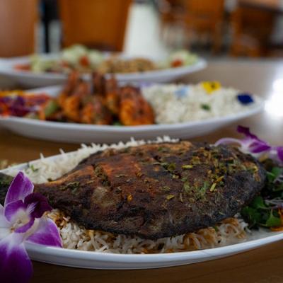Grilled whole fish served over rice, with other dishes in the background.