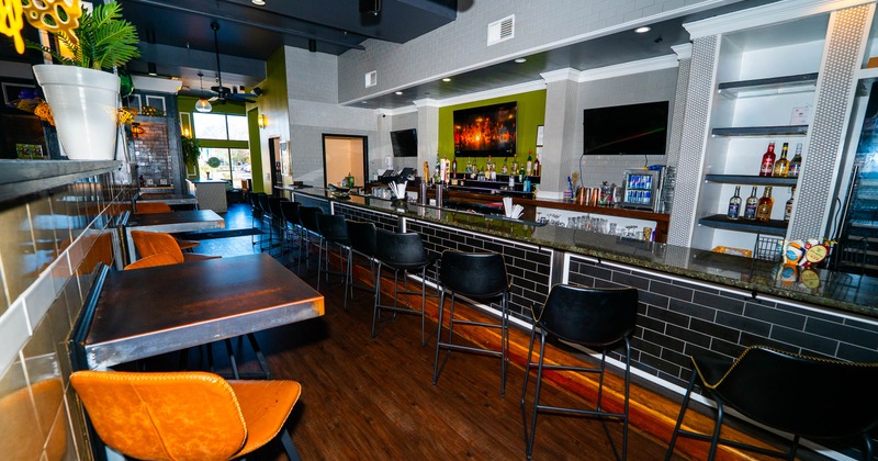 Modern bar interior with a sleek black counter, high-backed chairs, alcohol shelves