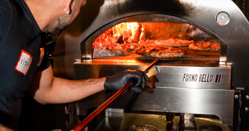 Pizza maker holding a peel with pizza inside an oven