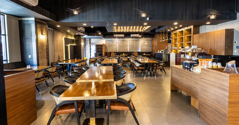 Interior seating area with wooden tables, black chairs and warm lighting