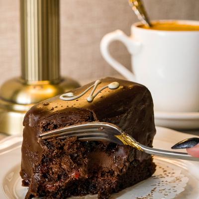 Chocolate cake being eaten with a fork, with cup of coffee in the background.