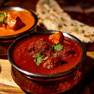 Bowl of lamb curry topped with herbs and served with naan bread.
