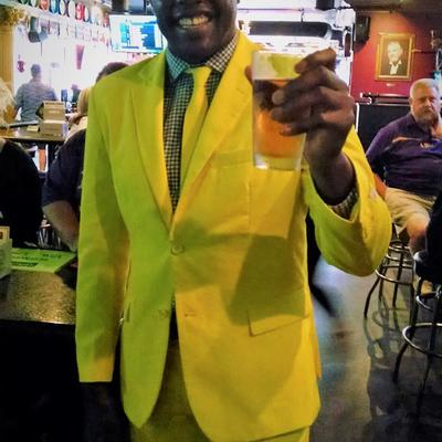 A smiling guy in a full yellow suit holding a beer