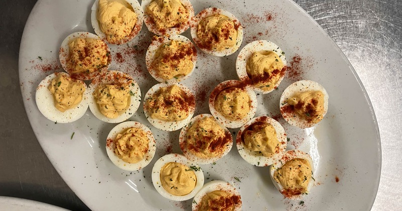 Deviled eggs topped with paprika on a white serving platter