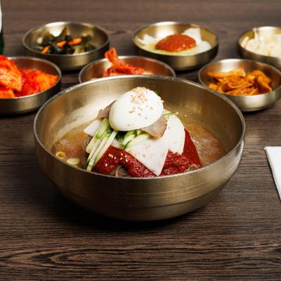 Buckwheat noodles with sweet and spicy red chili sauce, served alongside sides.