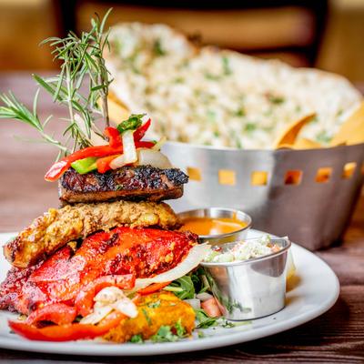 Stacked grilled meats and vegetables, garnished with rosemary, served with dipping sauces.