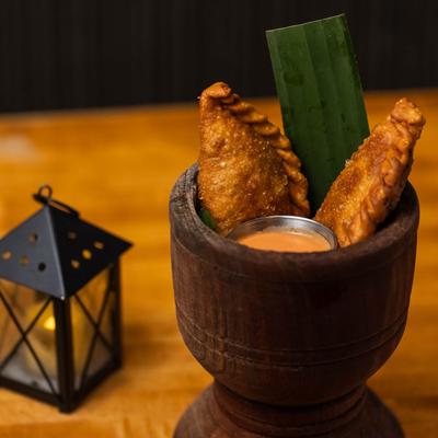 Two empanadas in a wooden cup with a side of sauce.