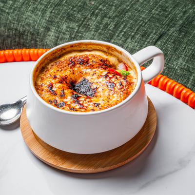 Creme Brulee served in a white ceramic mug set on a small wooden coaster.