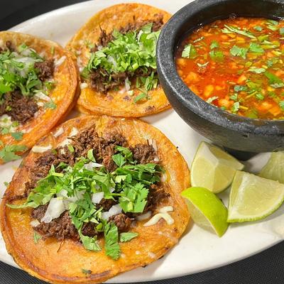 Three tacos topped with shredded beef, onions, and cilantro, served with salsa and lime.