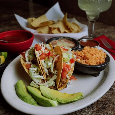 Ground beef tacos served with rice, beans, diping sauce and avocado slices.