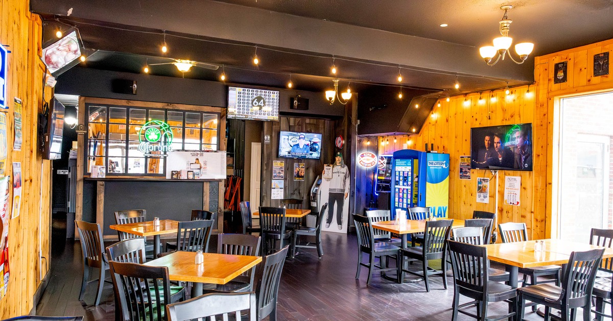A cozy restaurant interior with wooden walls, square tables, black chairs, a small bar