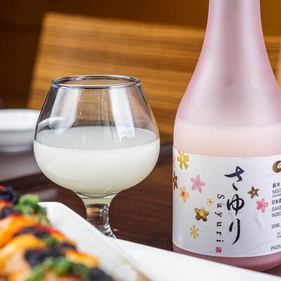 A glass of cloudy sake next to a bottle of sake with a floral label.