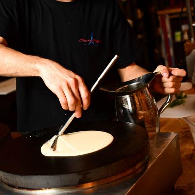 A person spreading crepe batter on a flat round griddle.