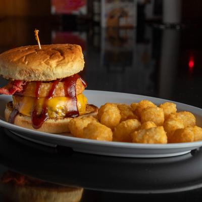 Bacon cheeseburger with onion ring, melted cheese, and sauce served with tater tots.