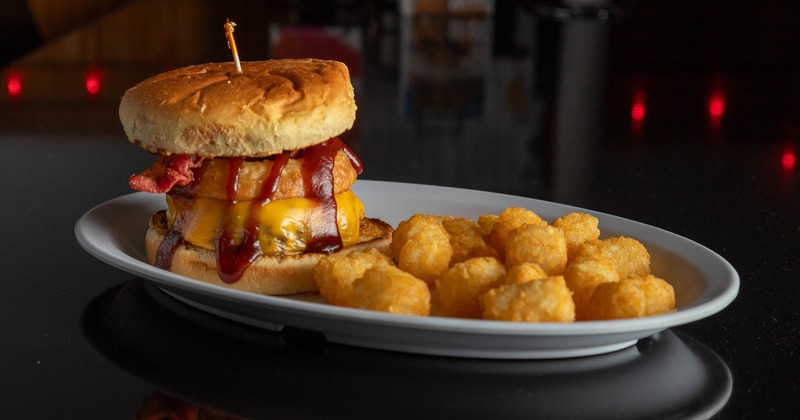 Bacon cheeseburger with onion ring, melted cheese, and sauce served with tater tots
