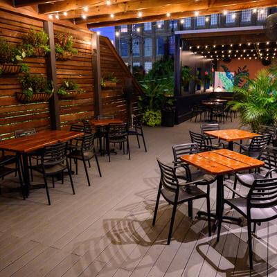 Outdoor patio seating with wooden tables, chairs, hanging plants, and string lights.