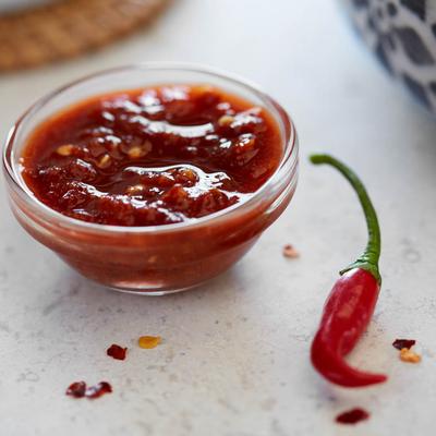 Red chili sauce in a bowl next to a red chili pepper.