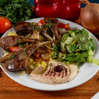 Grilled lamb chops served over rice with a fresh salad and hummus.