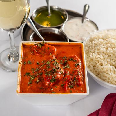 Butter chicken dish, on a table with white wine, rice, and chutneys.