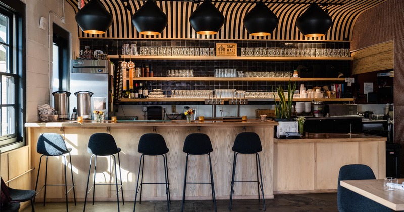 Modern bar with a light wood counter, black bar stools and large black pendant lights