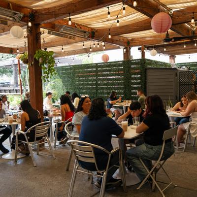 People enjoying food and drinks on a covered patio with string lights and paper lanterns.