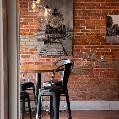 Interior, table and bar chairs in front of a rustic brick wall decorated with vintage pictures.