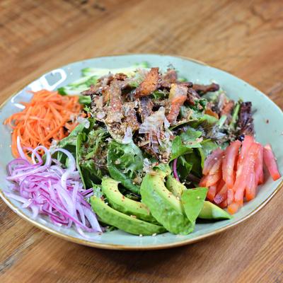 A colorful salad with topped with grilled meat.