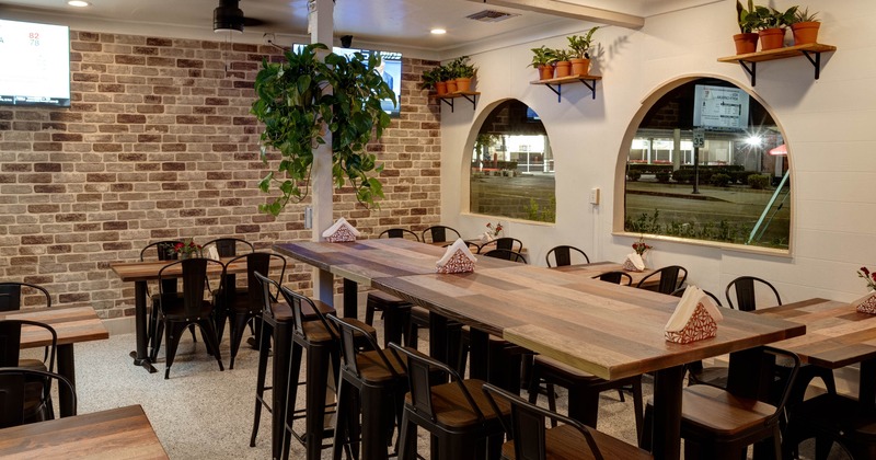 Interior, high seating table for ten, regular tables for four, arched windows, plant decoration