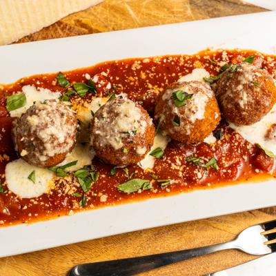 Arancini arranged over tomato sauce, topped with fresh basil.