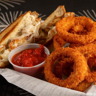 A grilled cheese sandwich with onion rings and a side of marinara sauce.