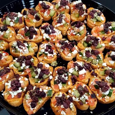 Platter of Mediterranean-style bruschetta topped with tomatoes, cheese, and olives.