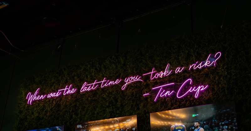 Neon sign on faux greenery reads When was the last time you took a risk