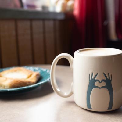 Mug of coffee served alongside pastry on a plate in the backgroung.