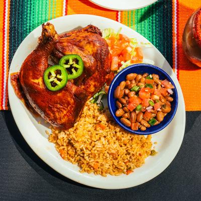 Pollo asado plate featuring a marinated half chicken topped with jalapenos, rice, and beans.