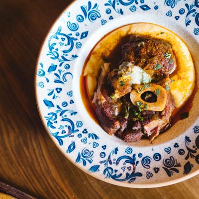 Braised meat on creamy polenta served on a decorative blue-patterned plate.
