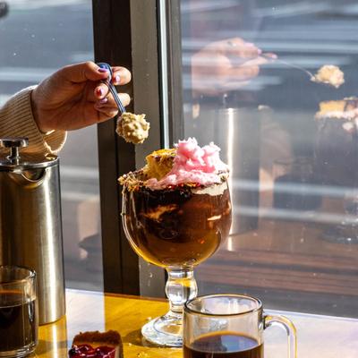 A hand lifting a spoonful of hot fudge sundae from a glass.