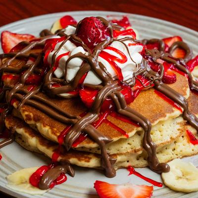 Nutella pancakes garnished with whipped cram, strawberry slices and strawberry syrup.