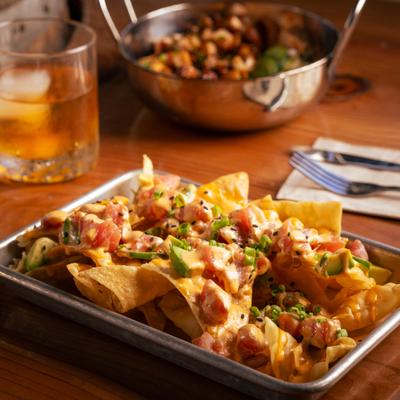 Tuna poke nachos on a tray beside a drink and another dish.