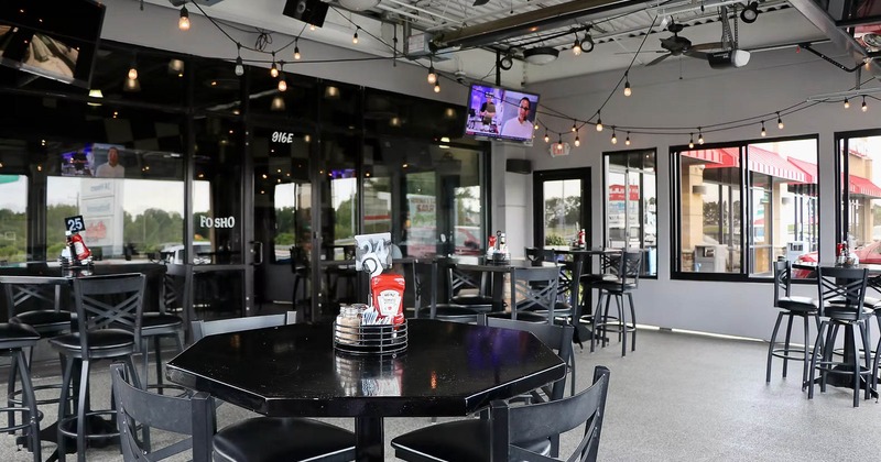Interior with black tables and chairs, large windows and ceiling string lights.