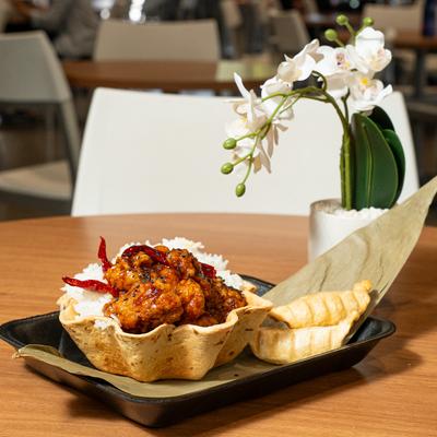 General Tso Chicken Rice Bowl on a wooden table with a white orchid.