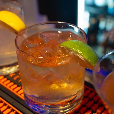 A close-up of a cocktail with ice and lime garnish on a bar.